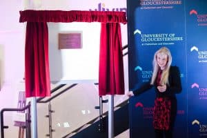 A woman reveals a brass plaque from behind red curtains.