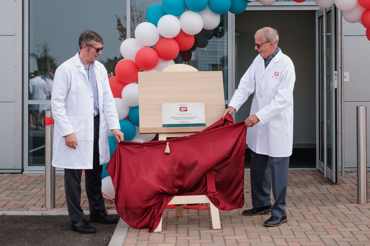 Two men unveiling a plaque from behind a red cloth.