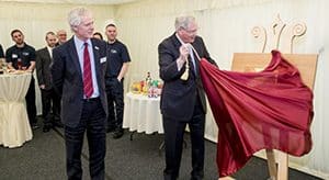 A man reveals an easel from under a red drape.