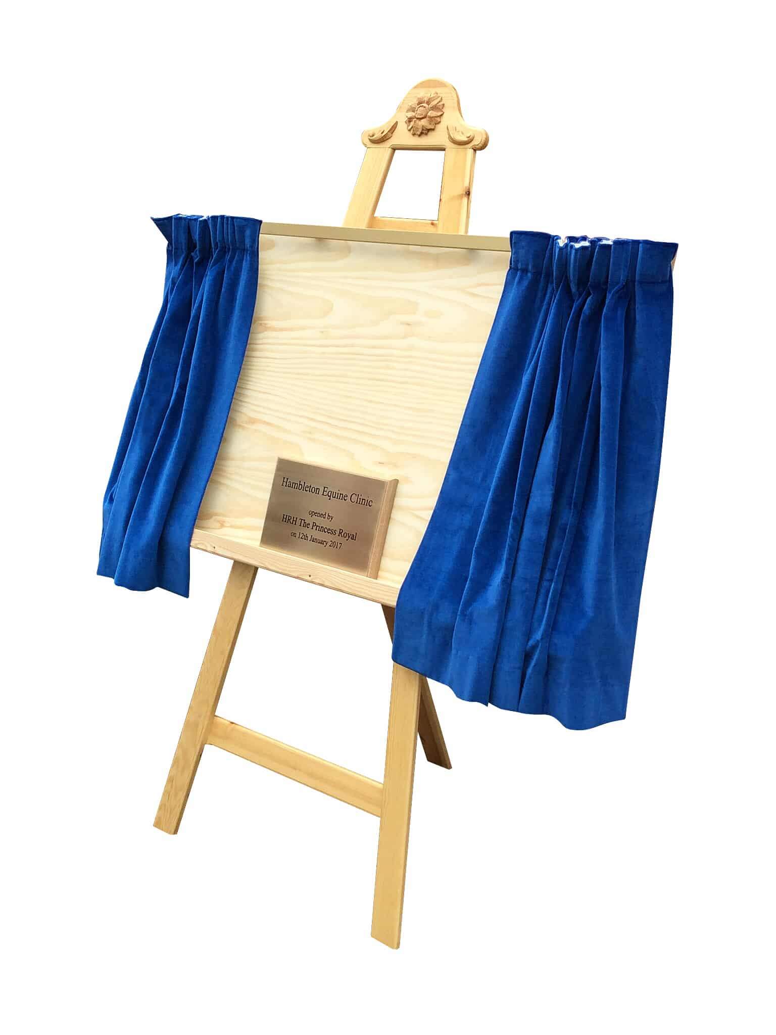 An easel with a brass plaque and blue curtains.