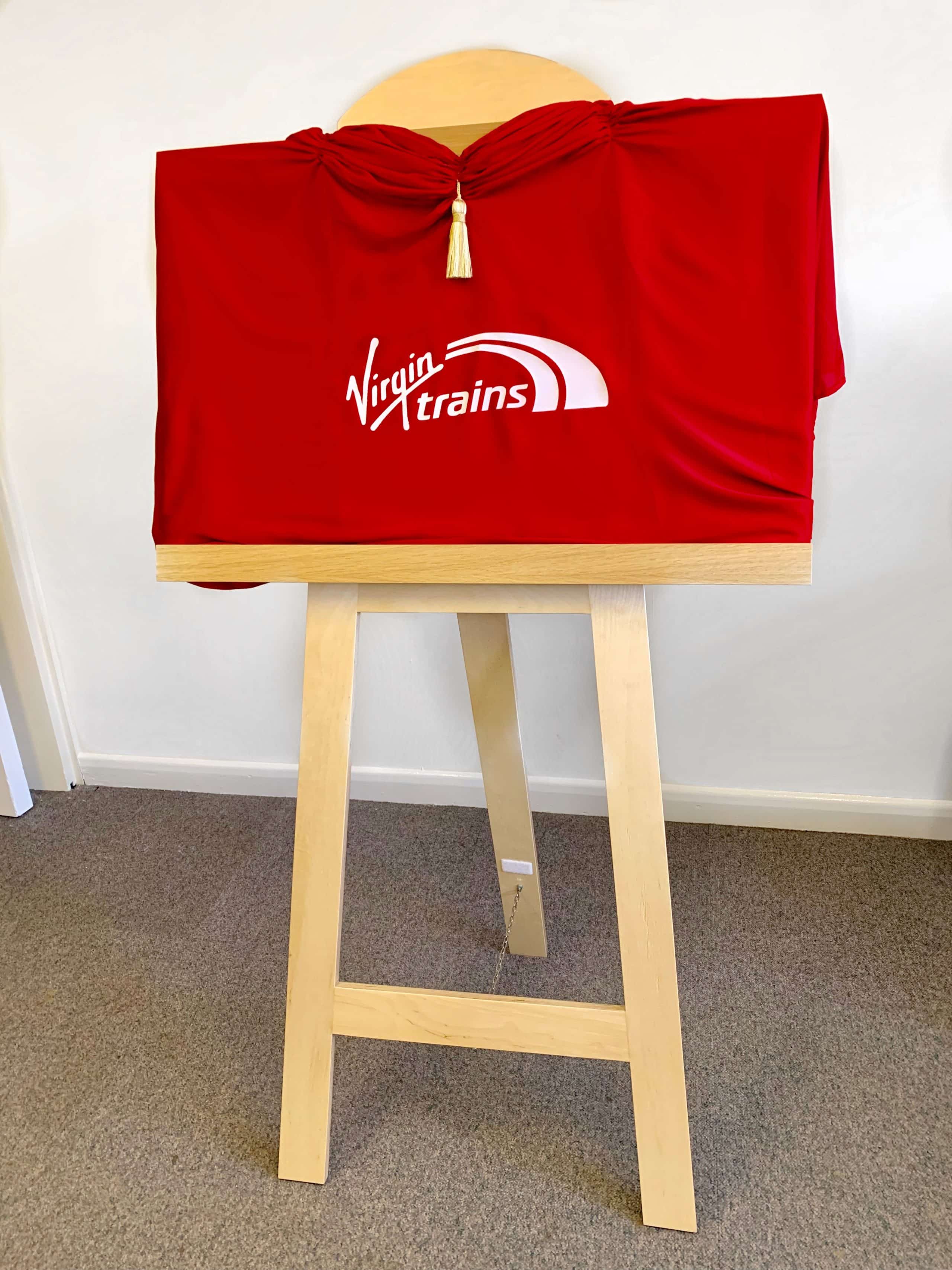 A red drape printed with the Virgin Trains logo covering an easel.