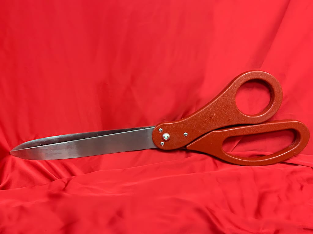 A pair of oversized red scissors on a red drape.