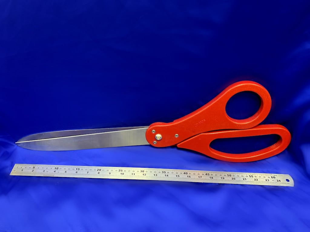 A pair of oversized red scissors next to a ruler showing they are two feet long.
