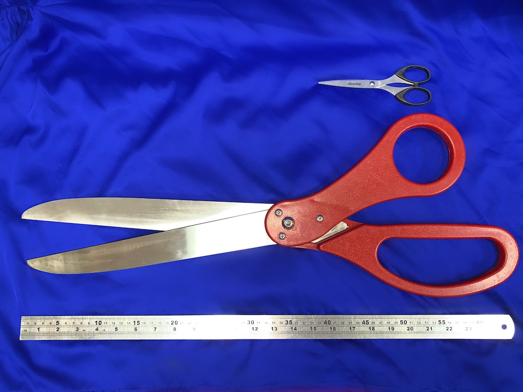 A pair of oversized red scissors next to a ruler showing they are two feet long, plus a pair of normal scissors for comparison.