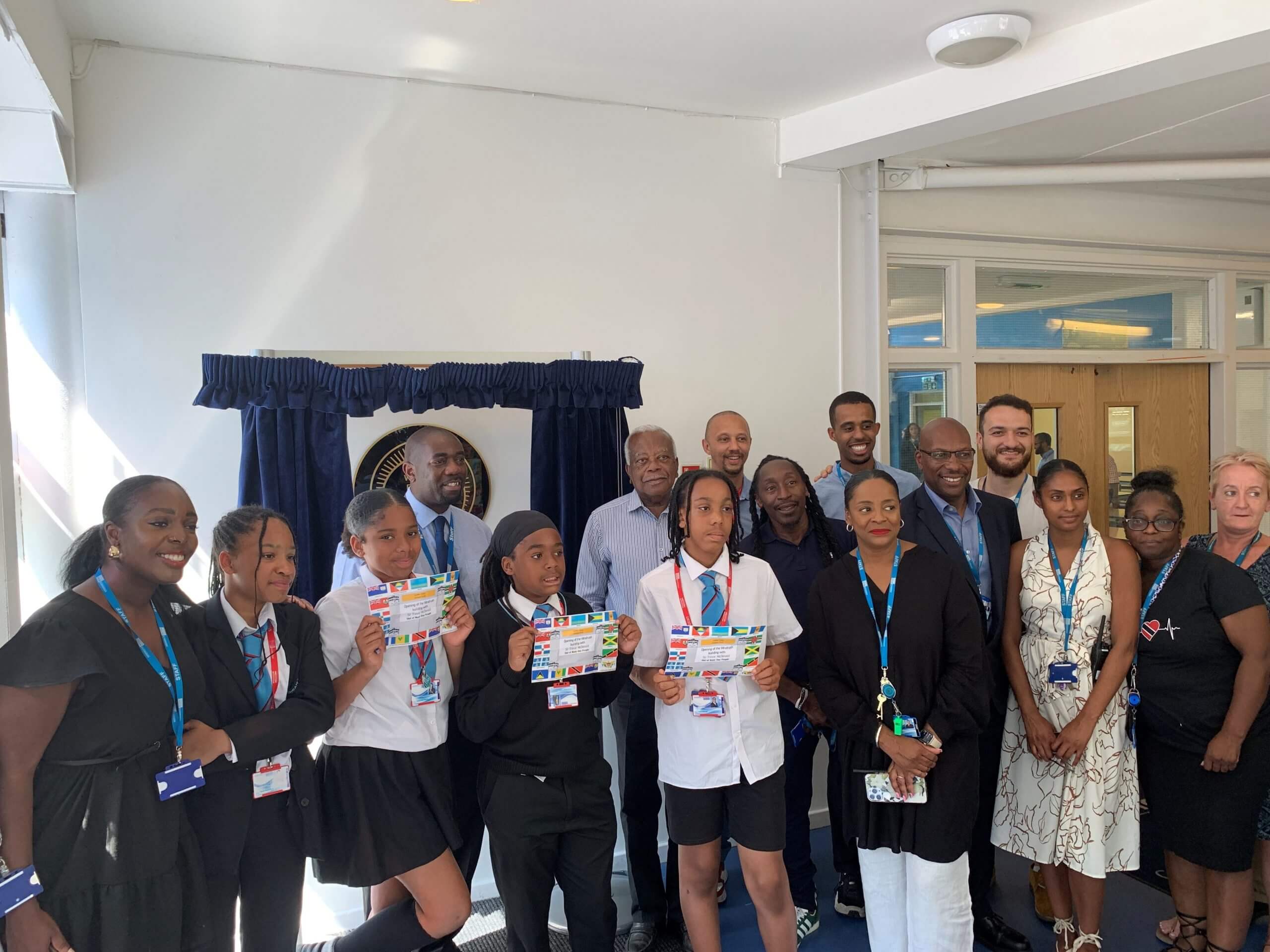 A group of students and adults standing in front of the plaque. Three of the children are holding certificates.