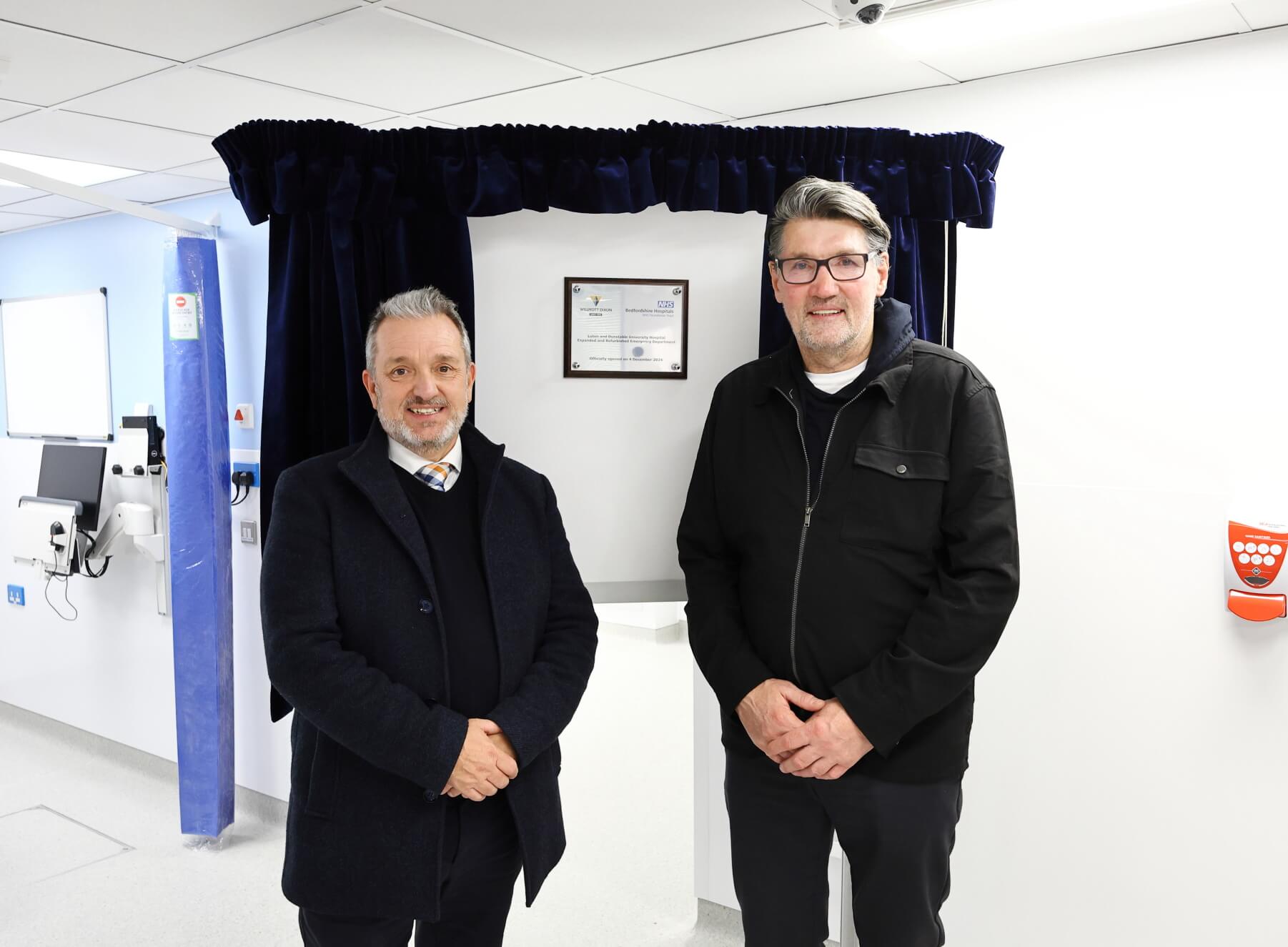 Two men standing in front of a silver plaque on an easel.
