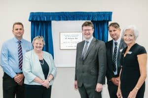 Five people stand in front of a plaque for the ATL Midlands Hub framed by blue curtains.