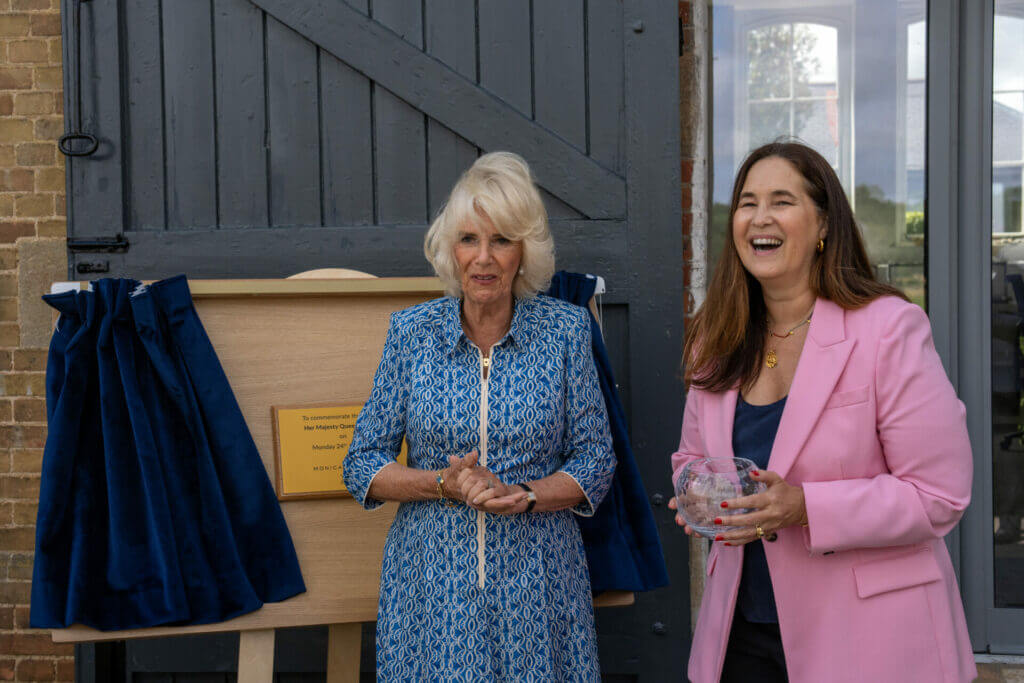 Two women standing in front of a plaque framed by blue curtains.