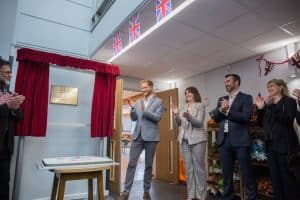 Some people applauding a plaque framed by red curtains.