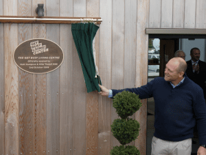 A man smiles at the Get Busy Living! Centre plaque.