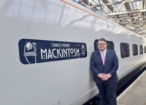 A man stands next to the Mackintosh graphic on the side of a train.