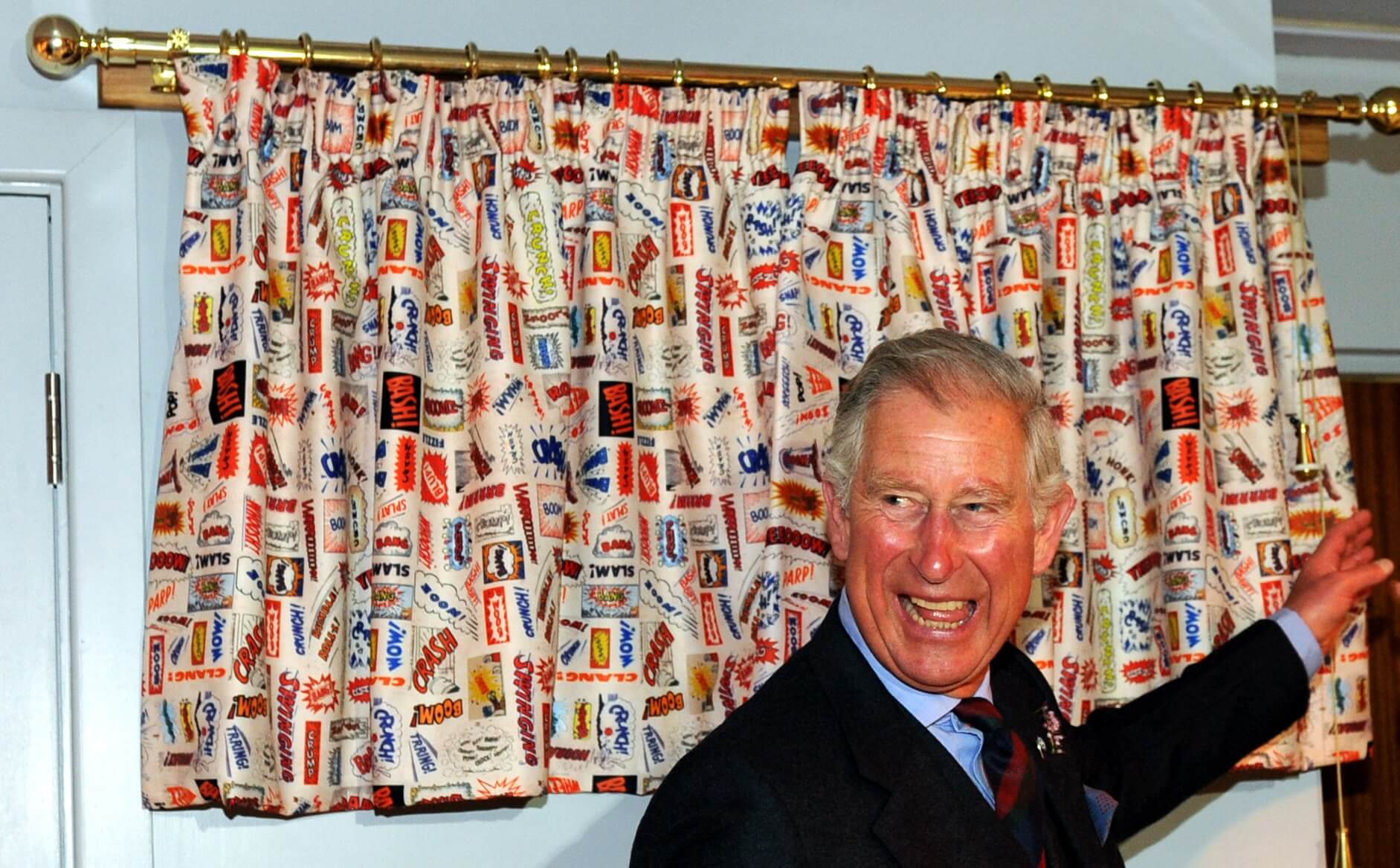 A man smiling in front of a pair of curtains printed all over with comic book sound effects.