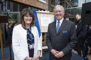 Two people pose in front of a plaque on an easel framed by blue curtains.